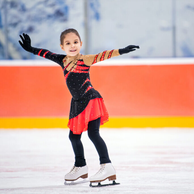 little girl figure skater in light pink tracksuit with smile skates on the ice on an indoor skating rink. little girl figure skater in a light pink tracksuit with a smile skates on the ice on an indoor skating rink.